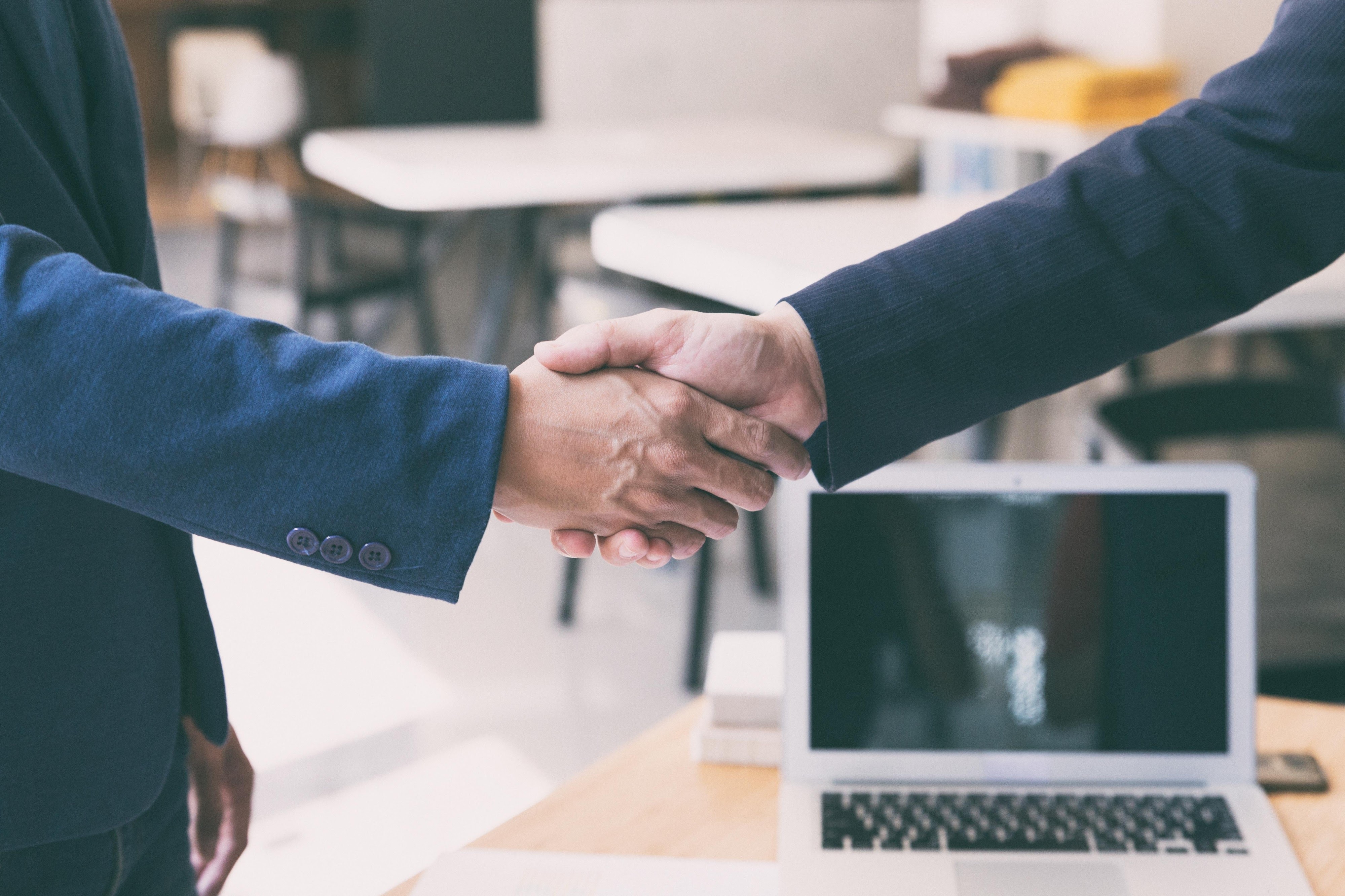 Image of two business people shaking hands over a laptop, symbolizing partnership and a tailored recruitment fit.